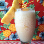A spiced piña colada garnished with pineapple in front of a tropical background.