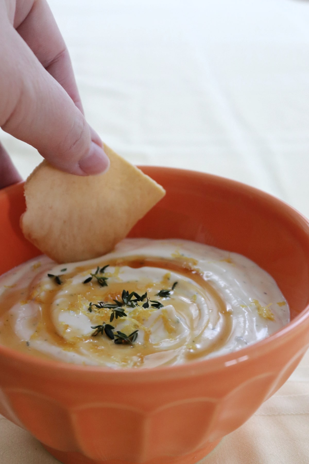 A hand dipping a pita chip into whipped honey ricotta.