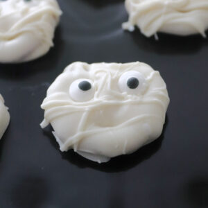 A pretzel covered in white chocolate with candy eyes to look like a ghost.