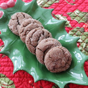 A close up image of chocolate ginger crinkle cookies on a holly plate sitting on a red and green holly cloth.