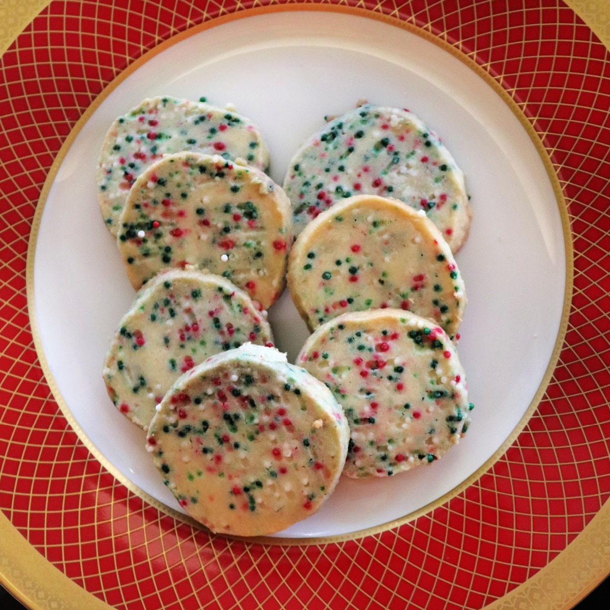 A close up image of 7 Christmas funfetti cookies on a red and gold plate.