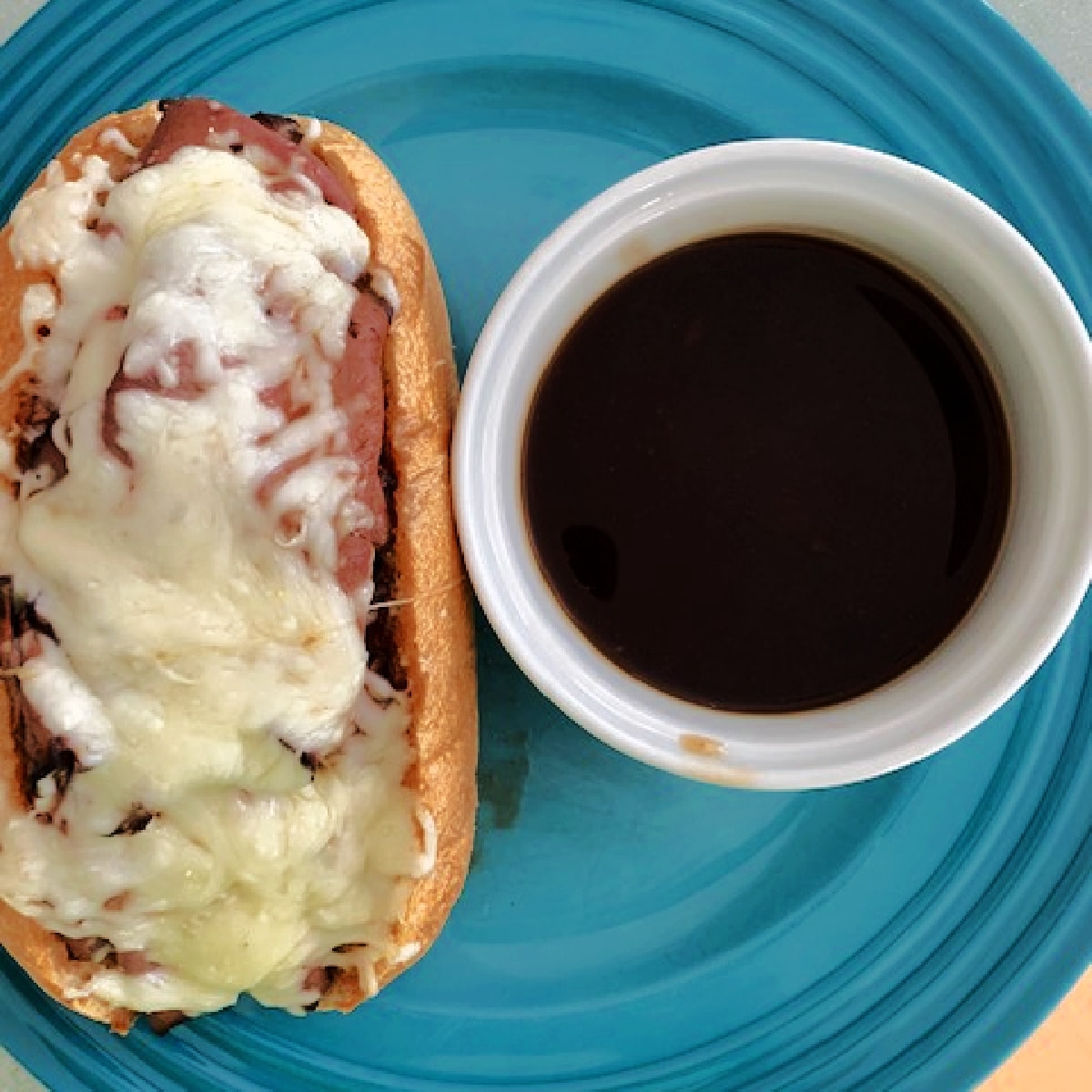 A French dip sandwich on a blue plate next to a bowl of au jus.