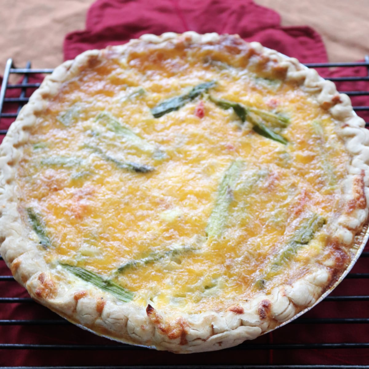 Whole asparagus and red pepper quiche on a cooling rack.