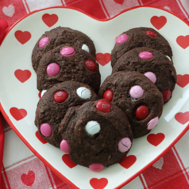 An overhead view of seven chocolate M&Ms cookies on a heart shaped plate.