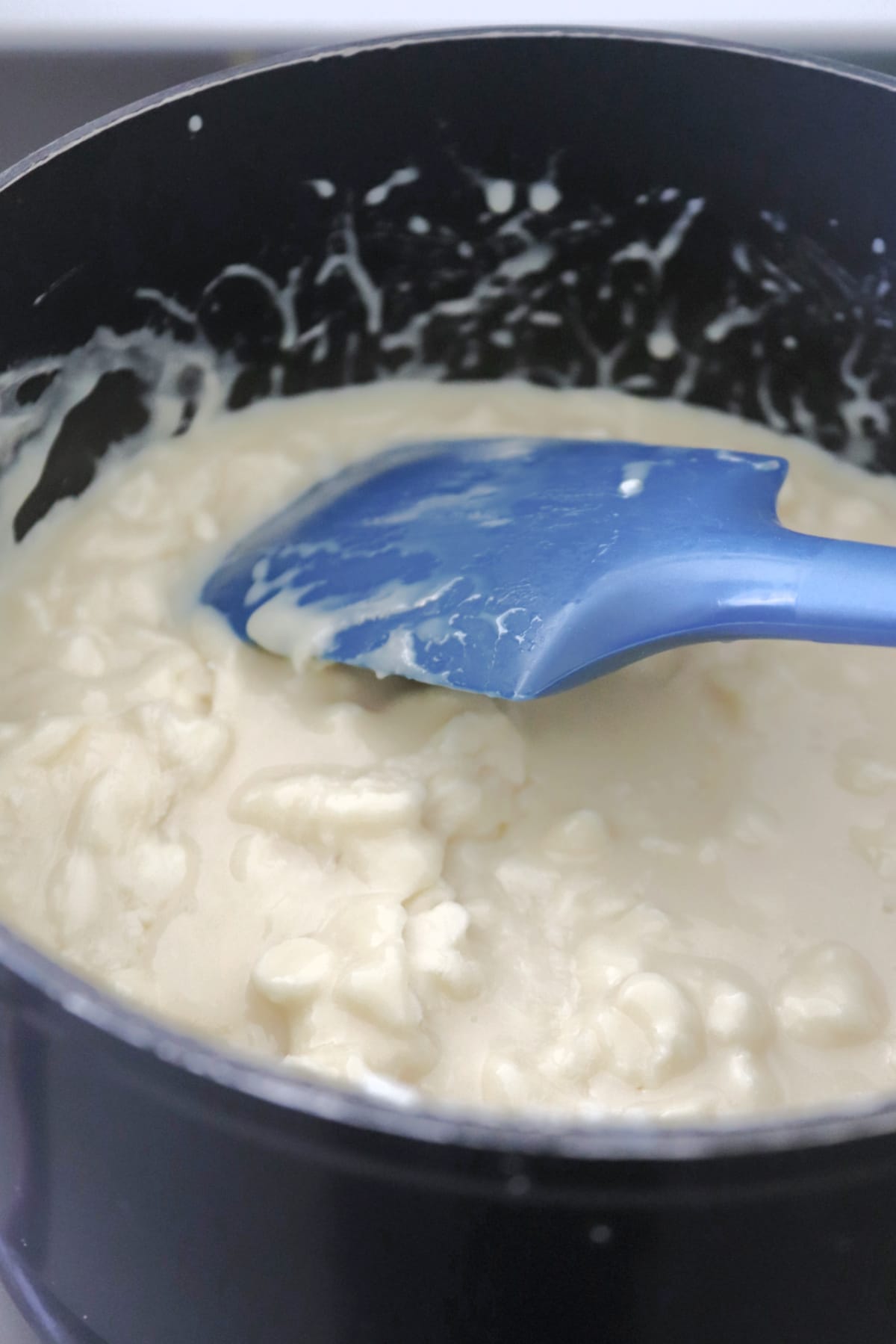 White chocolate chips melting in a saucepan with a blue spatula in the mixture.