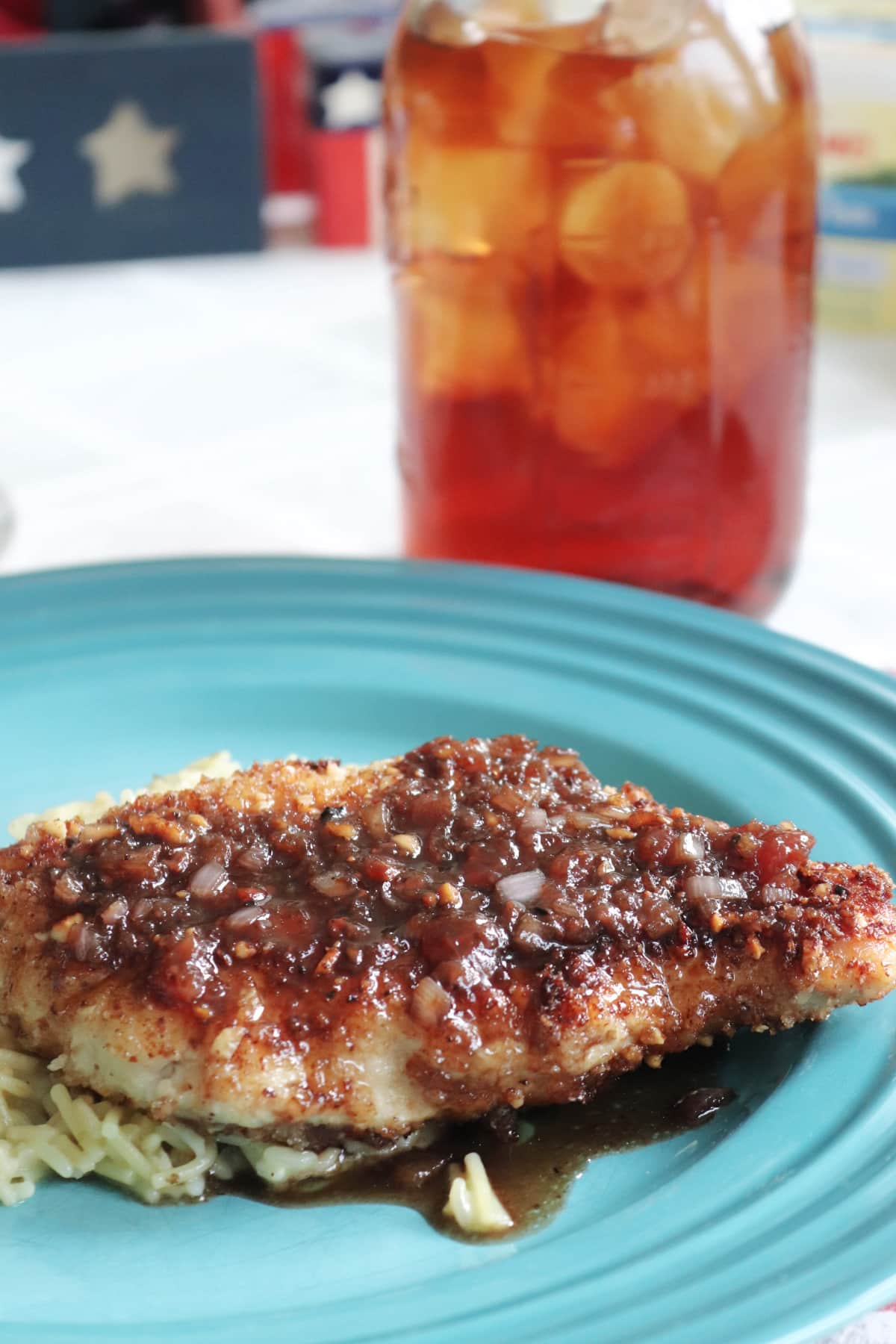 Almond Crusted Chicken with strawberry balsamic sauce on a blue plate with a glass of ice tea next to it.