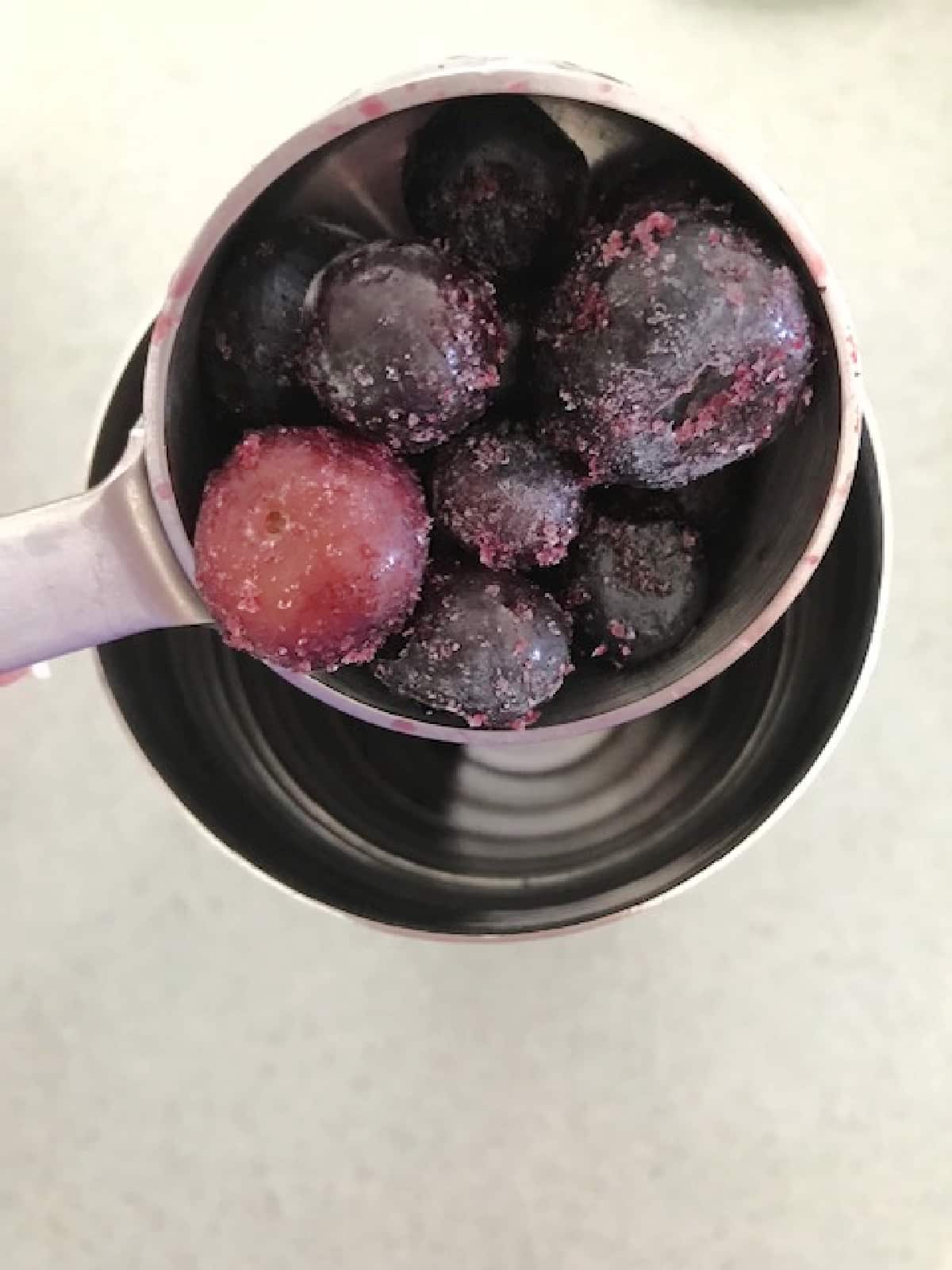 Blueberries in a measuring cup over a cocktail shaker for a blueberry margarita recipe.