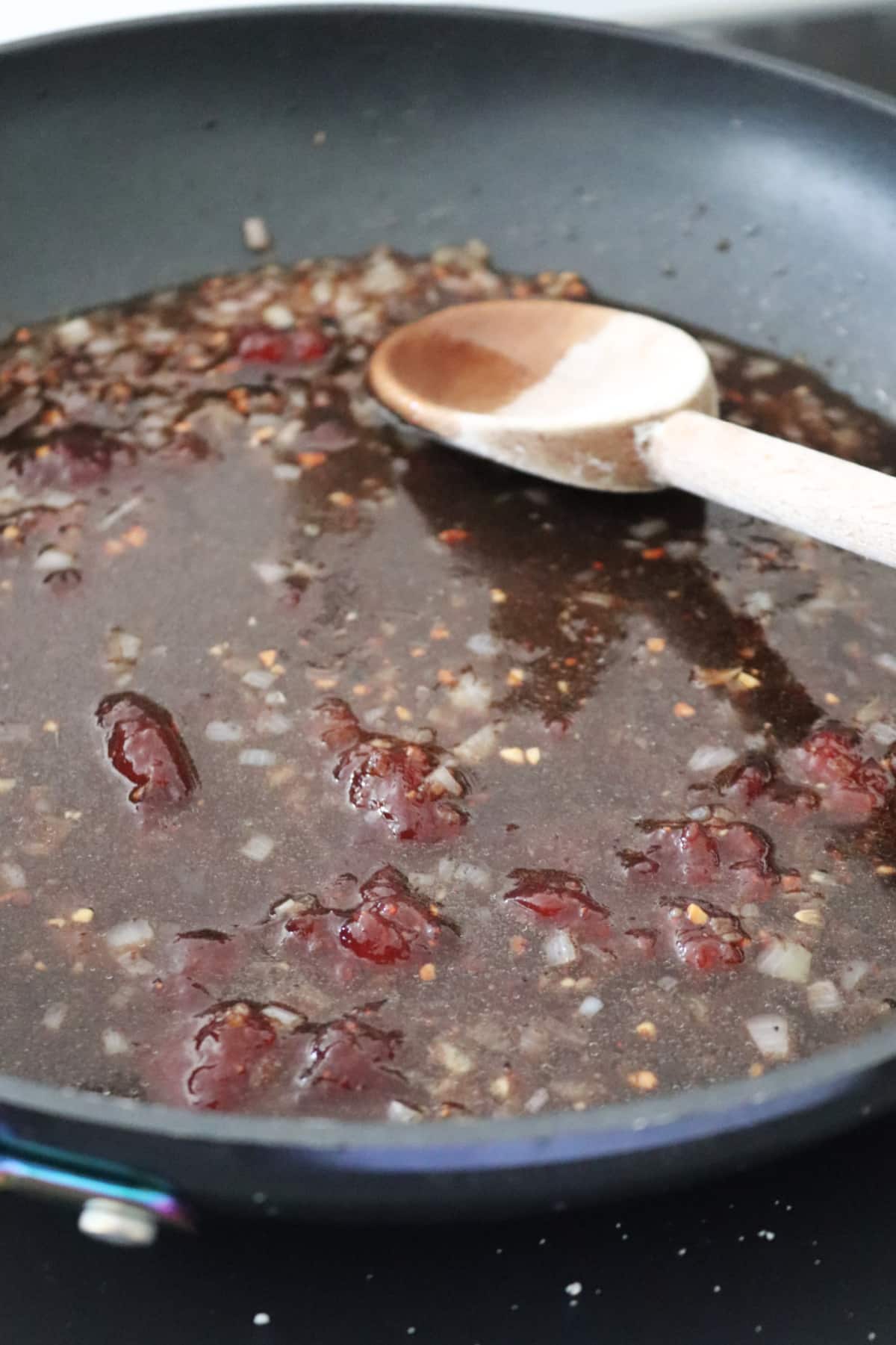 Strawberry balsamic sauce in a skillet with a wooden spoon resting in the skillet.