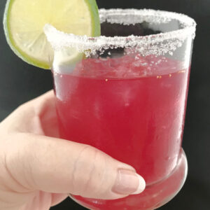 A blueberry margarita with sugar on the rim and a lime garnish being held.