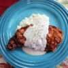 Overhead view of chicken fried chicken with apple cider gravy on a blue plate next to mashed potatoes.