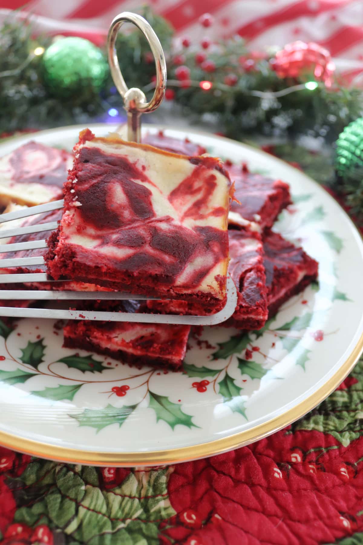 Red velvet cheesecake bars on a spatula being held over a plate with more bars on it.