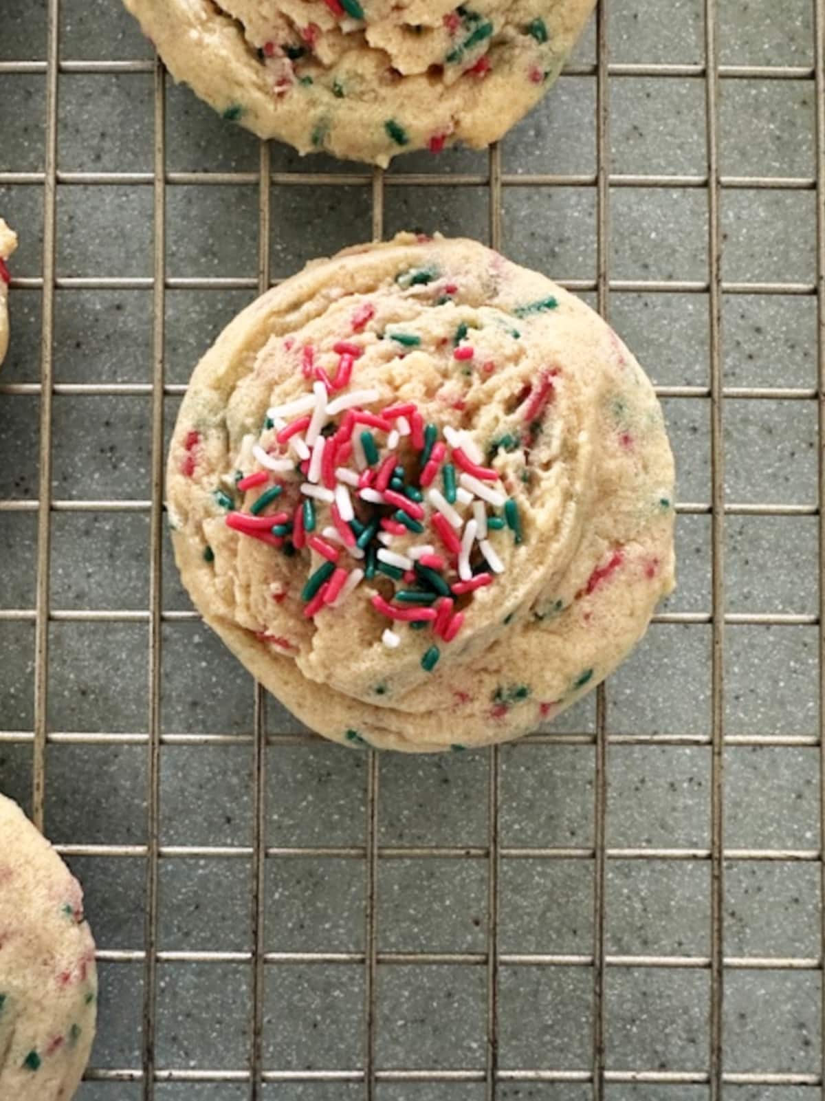 Overhead view of a vanilla pudding cookie with Christmas sprinkles on a baking rack.