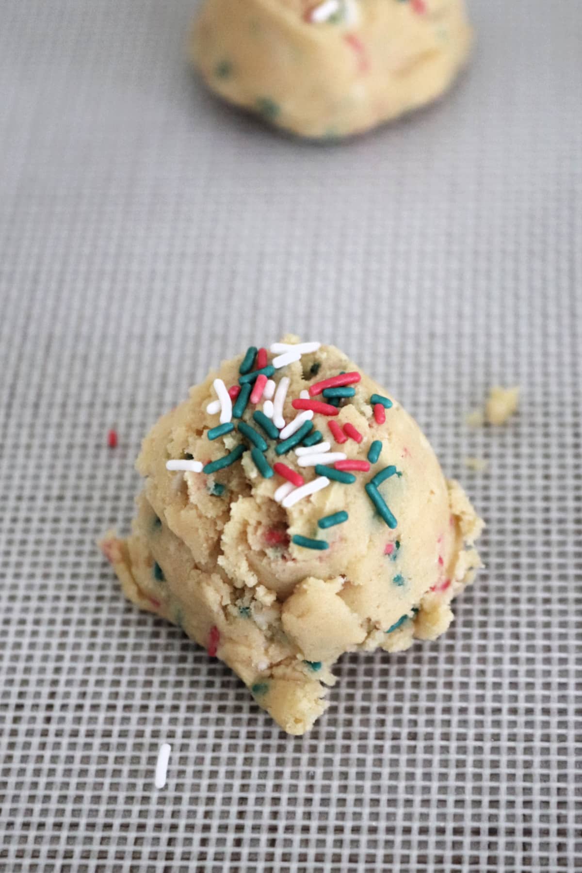 A cookie dough ball with Christmas sprinkles on a baking sheet.