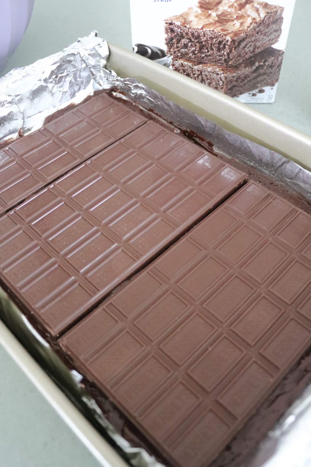 Chocolate bars on top of brownie batter in a pan.
