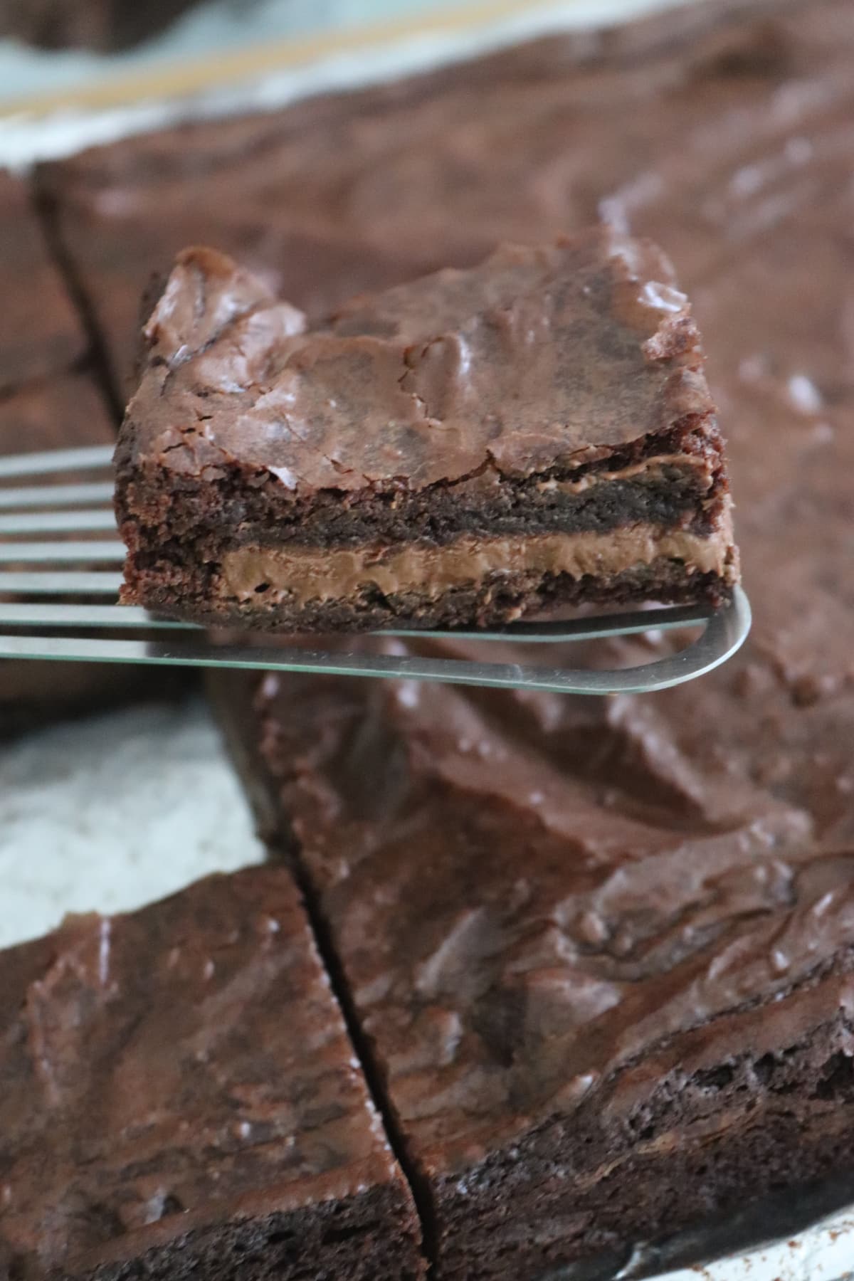 A slice of chocolate stuffed brownie on a spatula over a pan of brownies.
