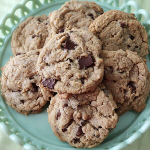 Overhead view of chocolate chunk cookies on a green cake plate.
