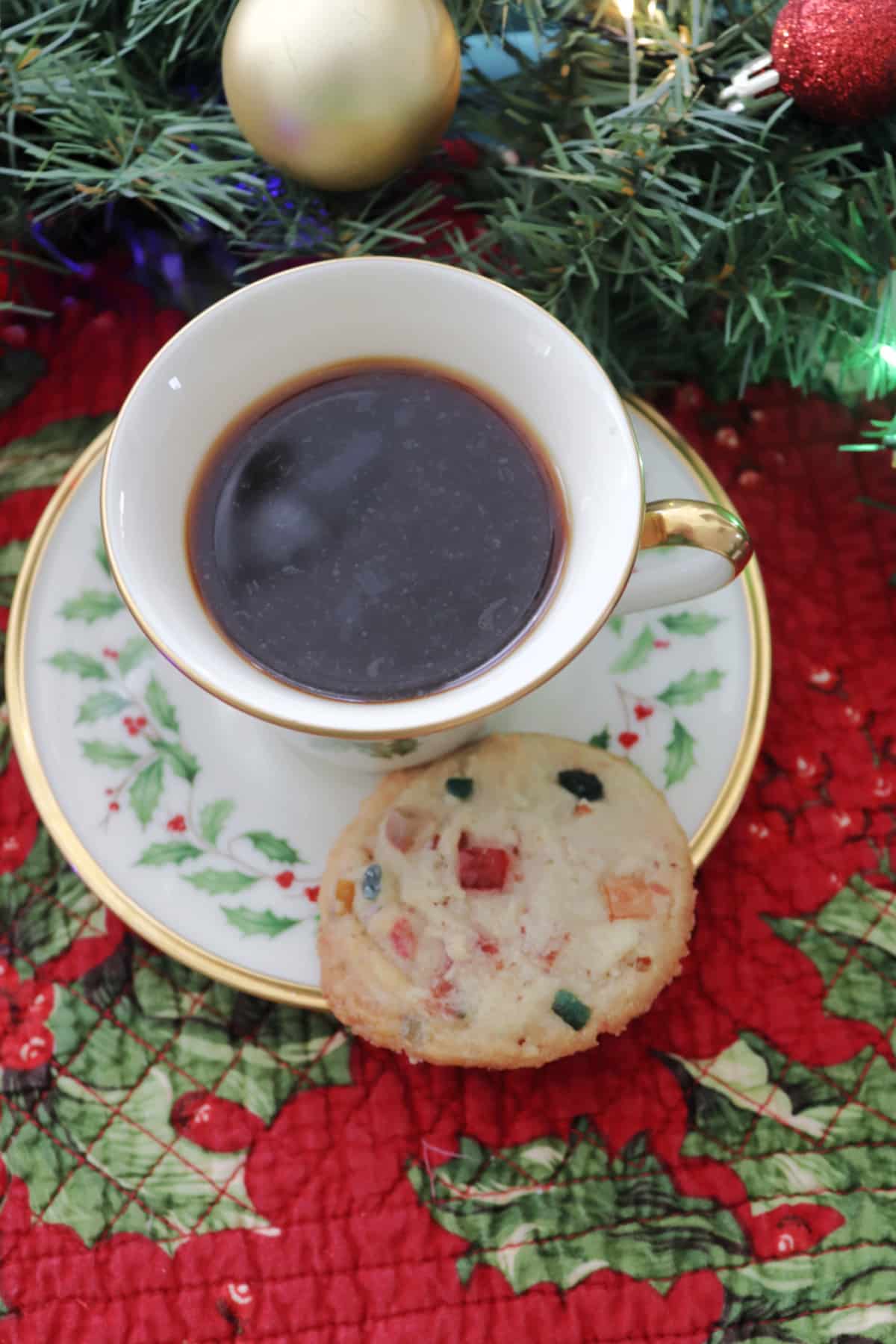 A fruitcake cookie on the saucer of a cup of coffee with Christmas decorations.