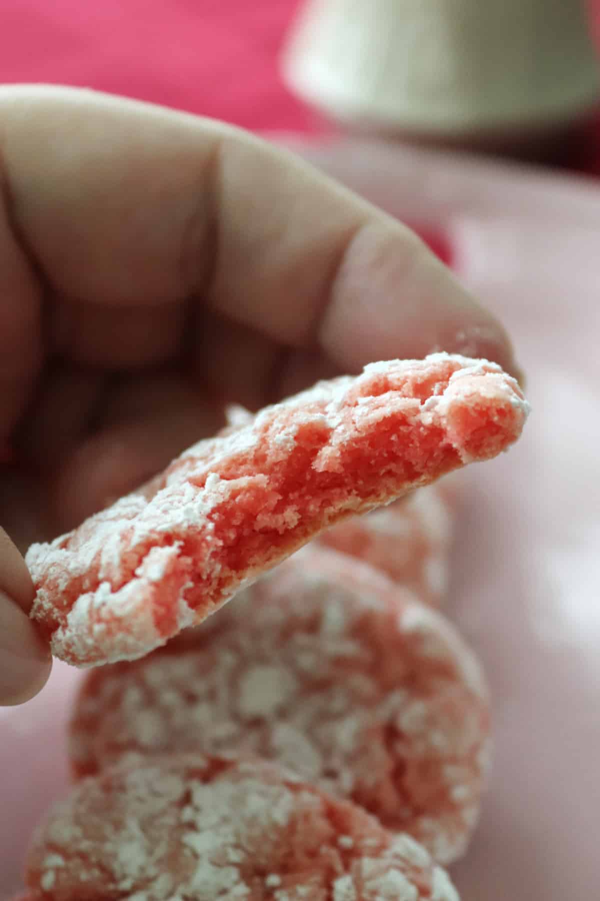 A strawberry crinkle cookie with a bite taken out of it.