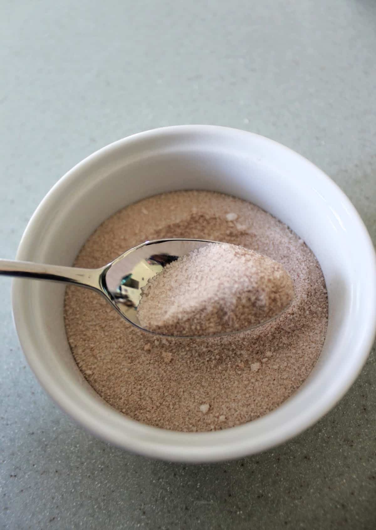 Cinnamon sugar on a spoon over a bowl.