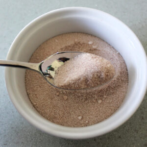 Cinnamon sugar on a spoon with more in a white ramekin.