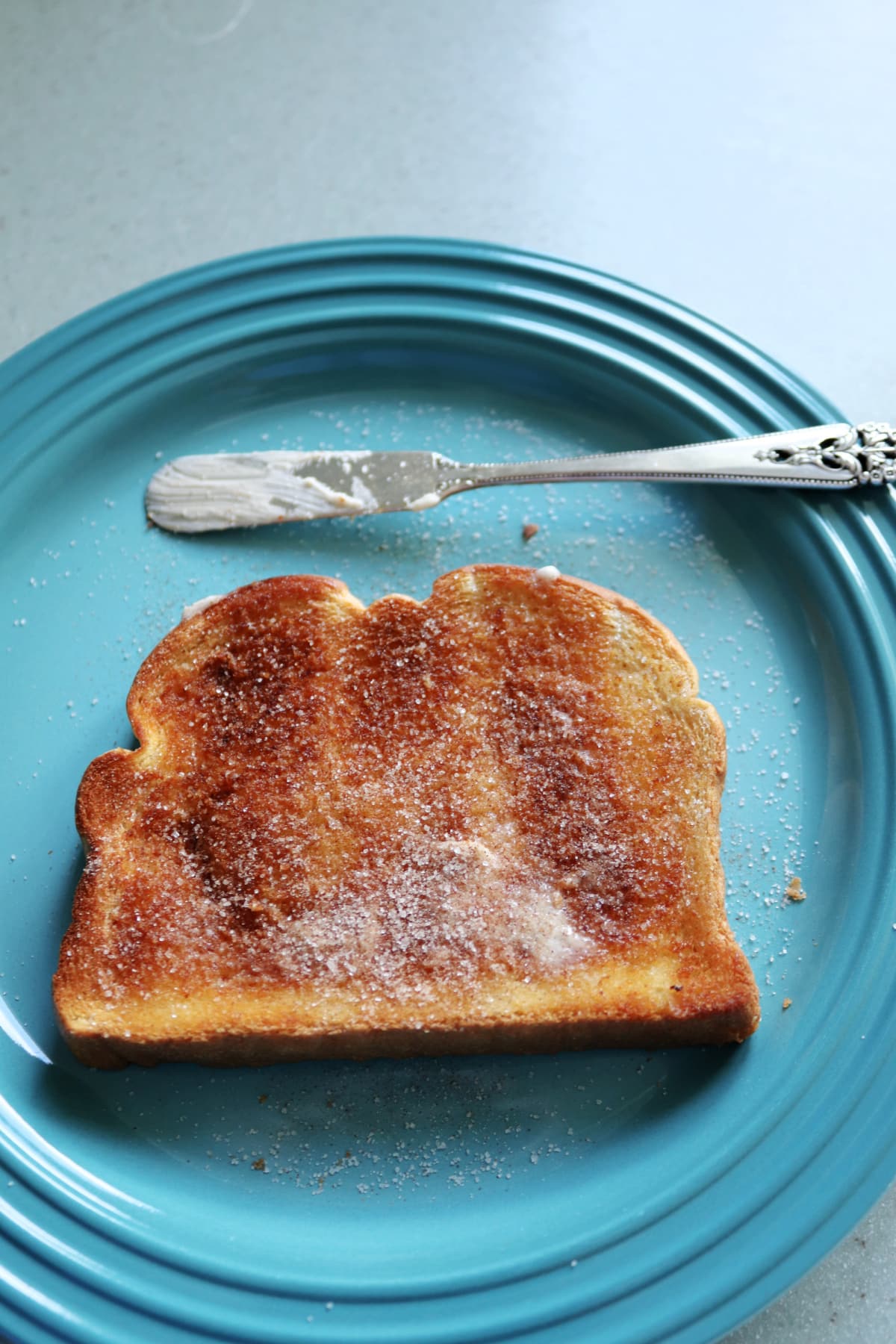 A piece of cinnamon toast on a blue plate with a butter spreader next to it.