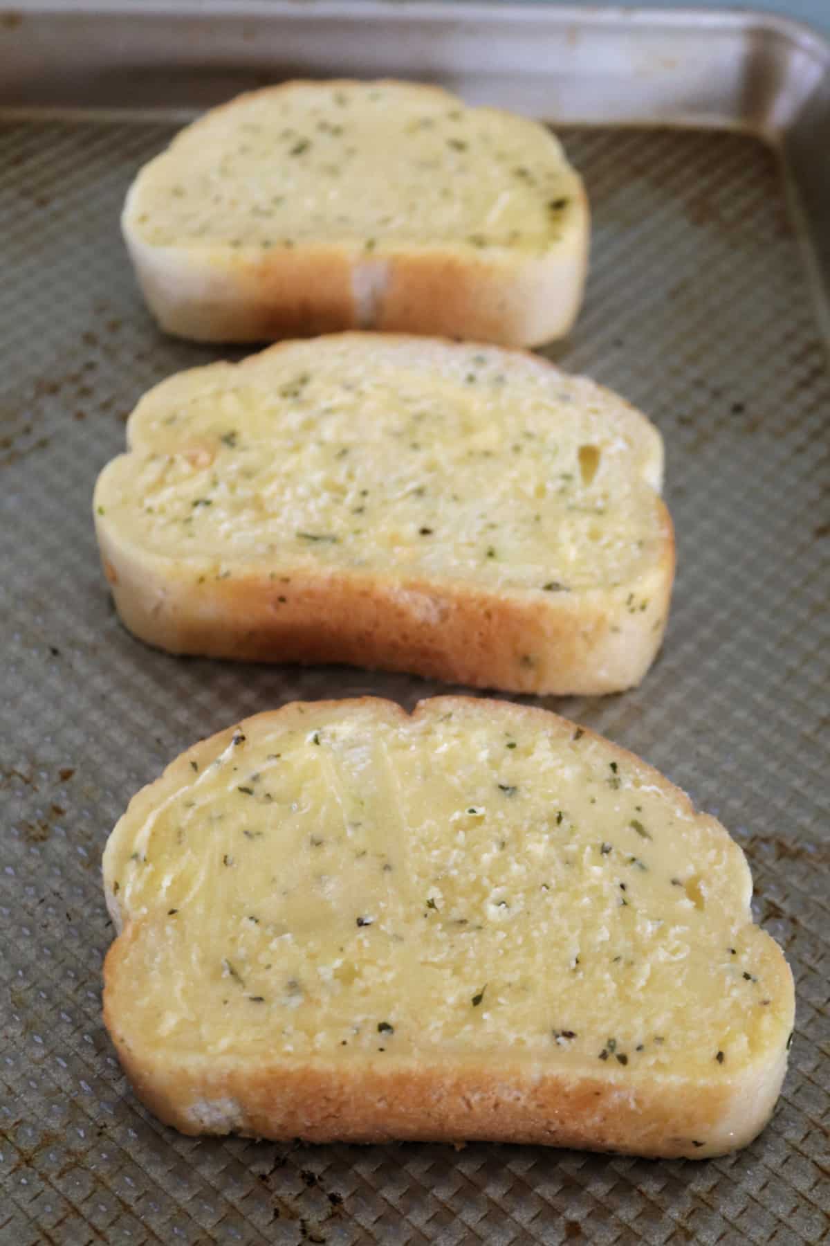 Three slices of garlic toast on a sheet pan.