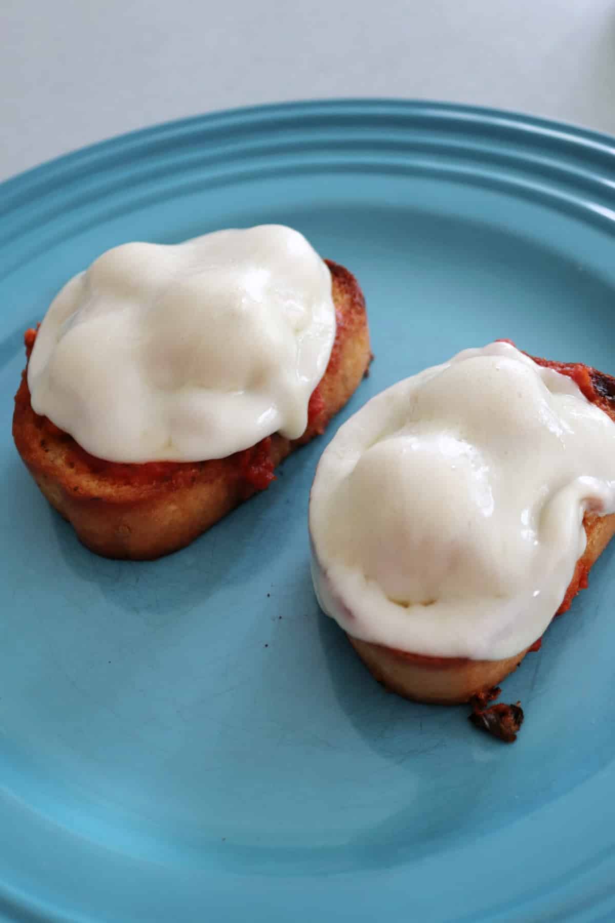 Two open faced meatball sandwiches on a blue plate.