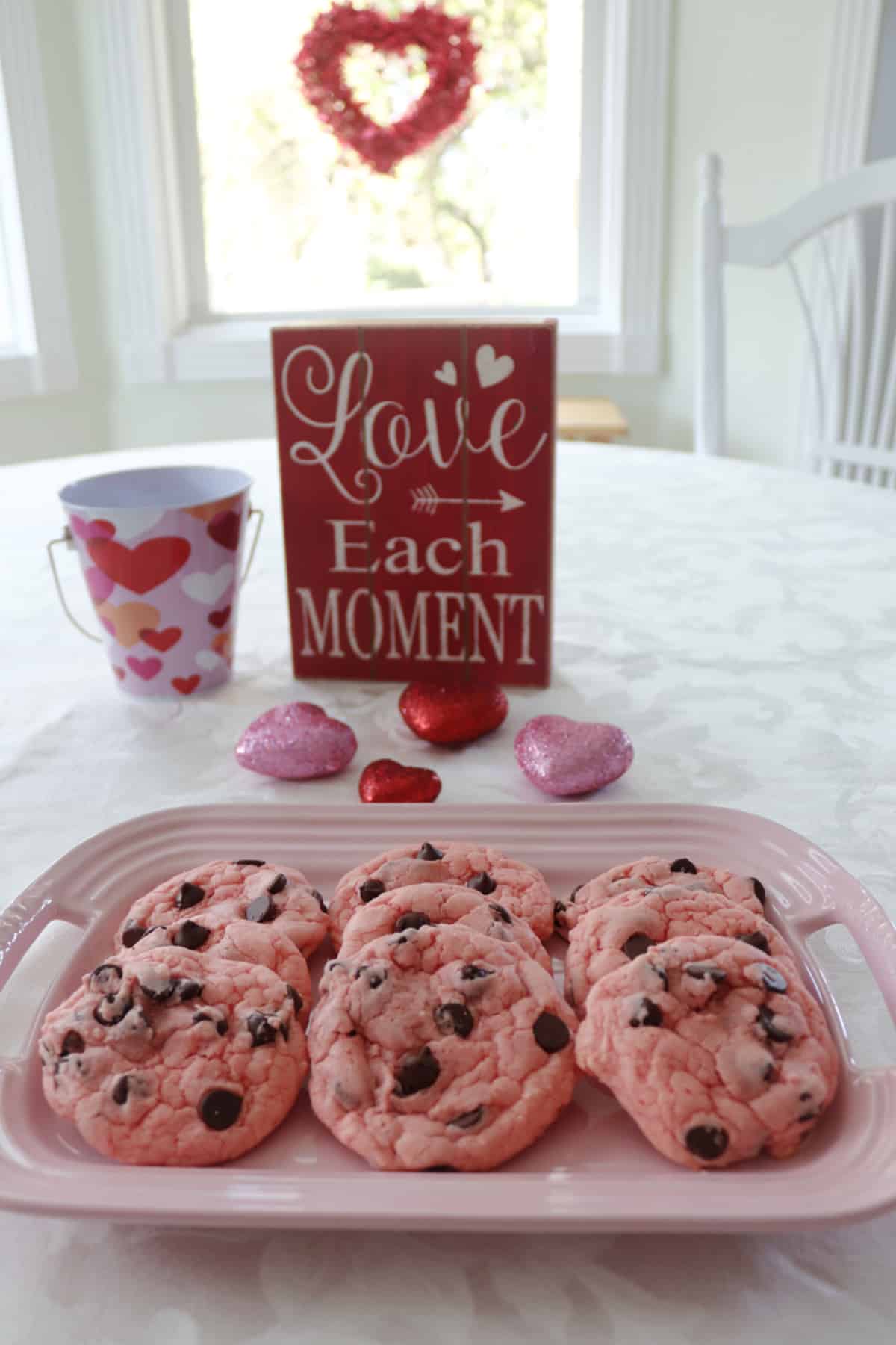 Strawberry chocoalte chip cookies on a pink platter with Valentine decorations around it.