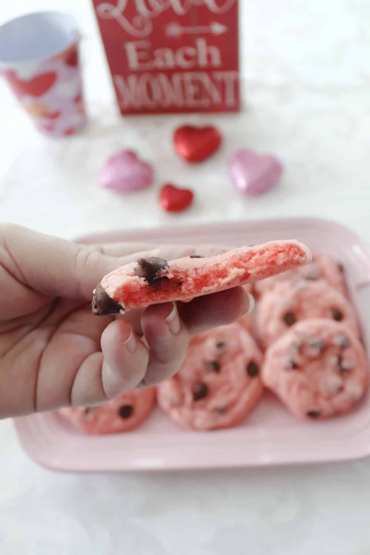 Half of a strawberry chocolate chip cookie showing the inside with a platter of cookies behind it.
