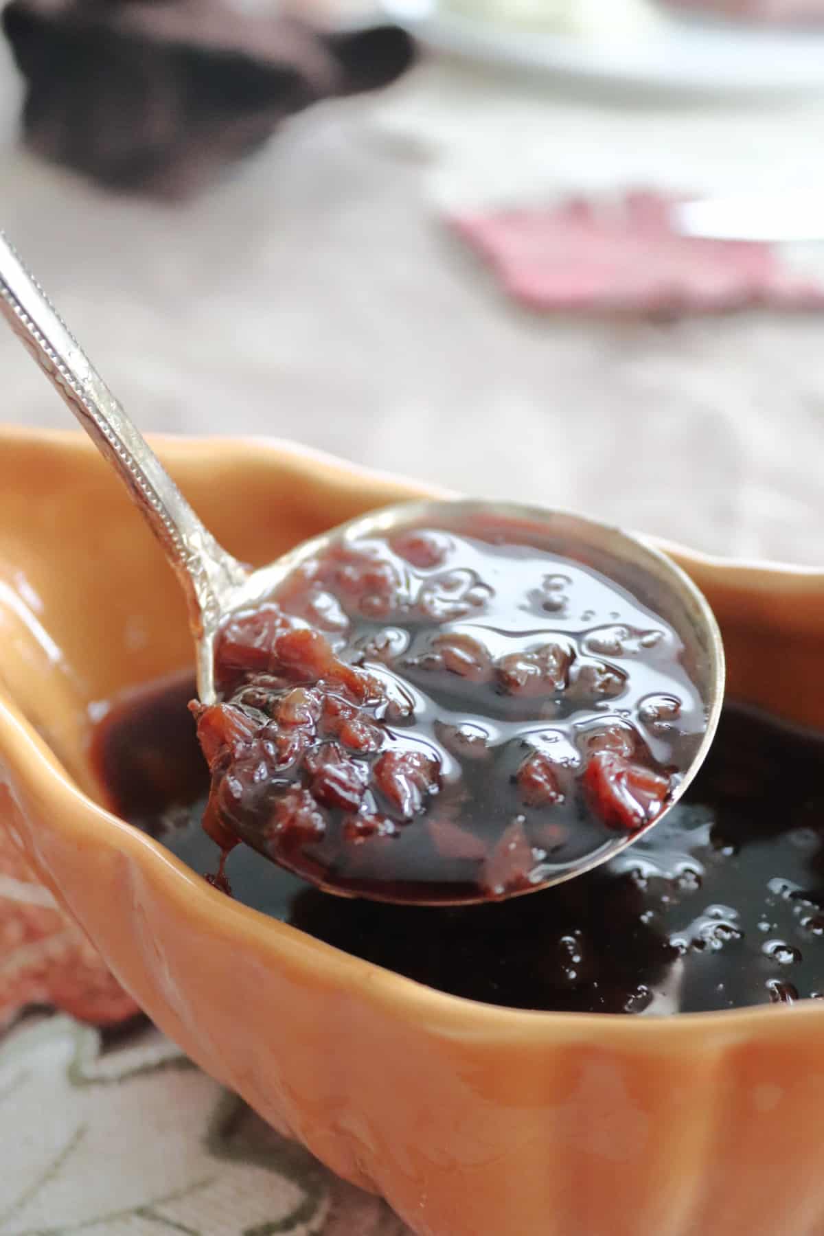 Raisin sauce on a ladle over a gravy boat with more sauce in it.