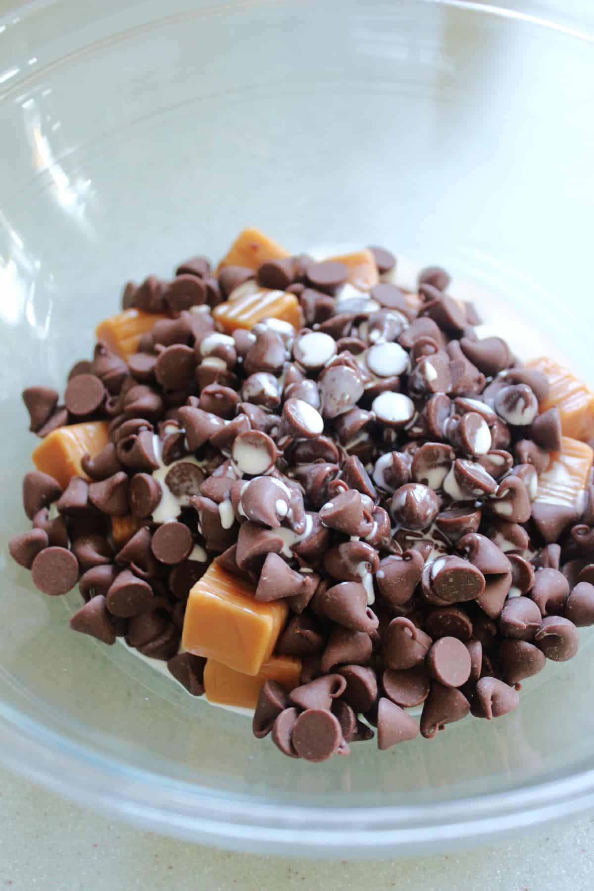Chocolate chips, caramels, and cream in a glass bowl.