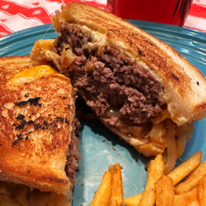 A Caramelized Onion Patty Melt on a plate next to shoestring French fries.