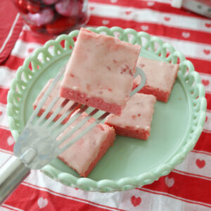 A glazed strawberry bar on a spatula over a plate with more bars.