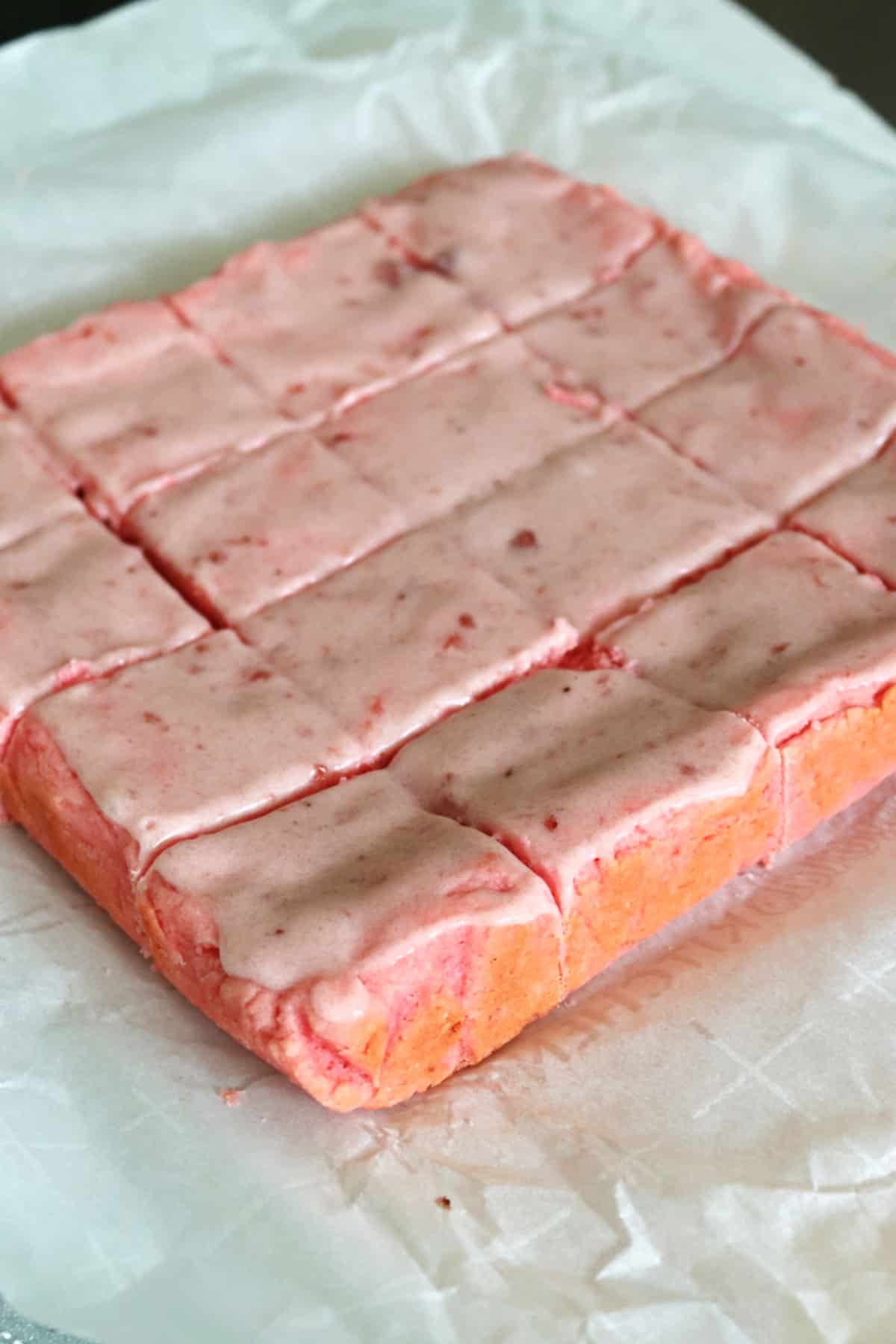 Glazed strawberry bars on a piece of parchment, cut into sections.