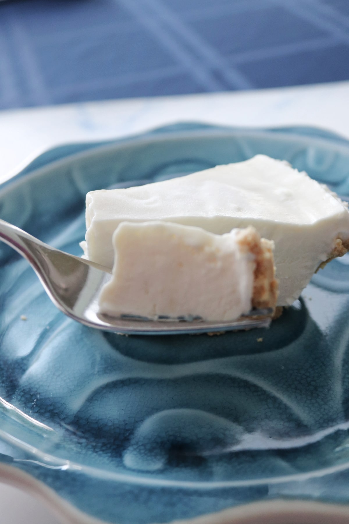 A bite of frozen Key lime pie on a fork next to a slice of pie on a blue plate.