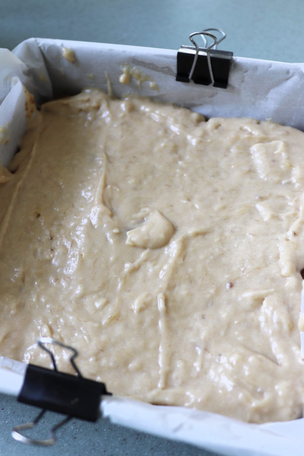 Batter in a baking pan lined with parchment and held by metal clips.