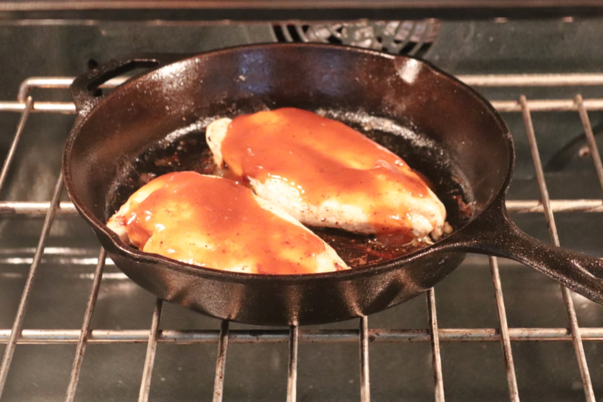 BBQ chicken in a cast iron skillet on an oven rack.