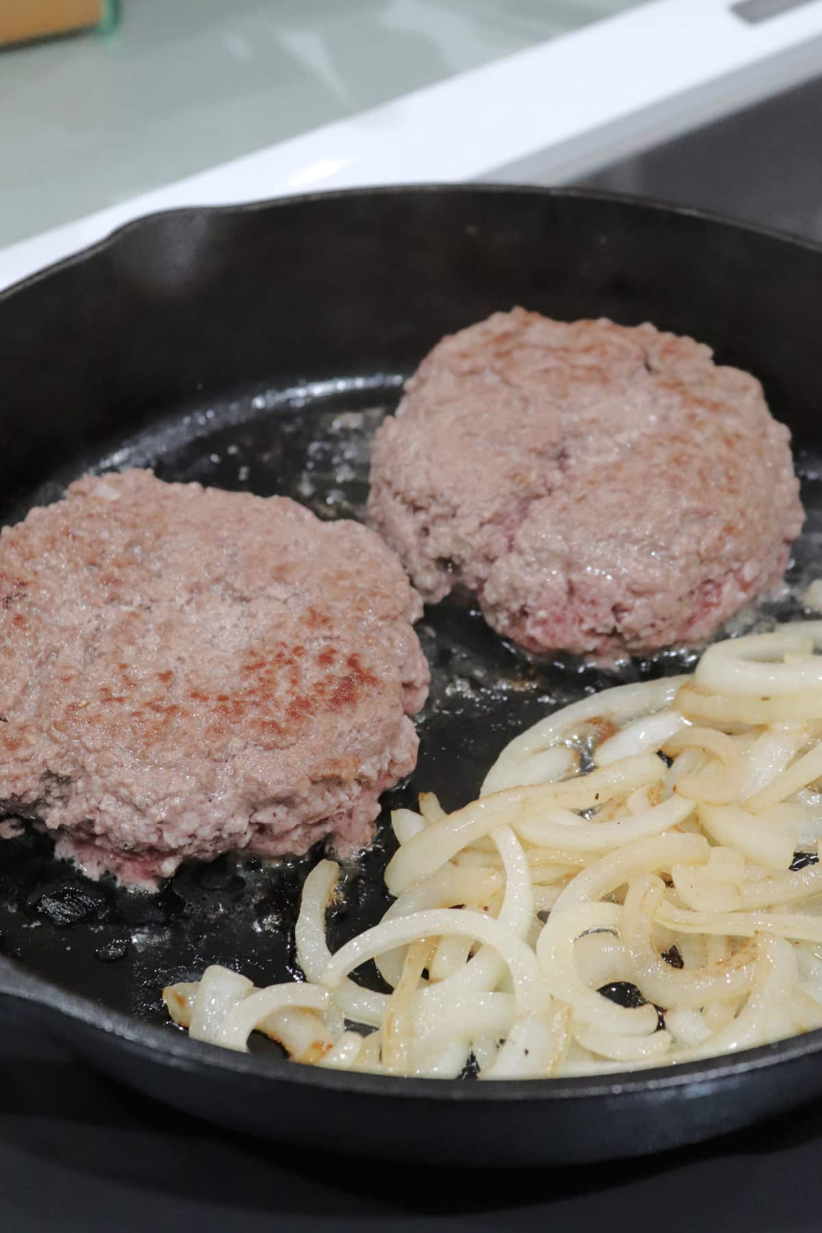 Two hamburger patties and sliced onions in a cast iron skillet.