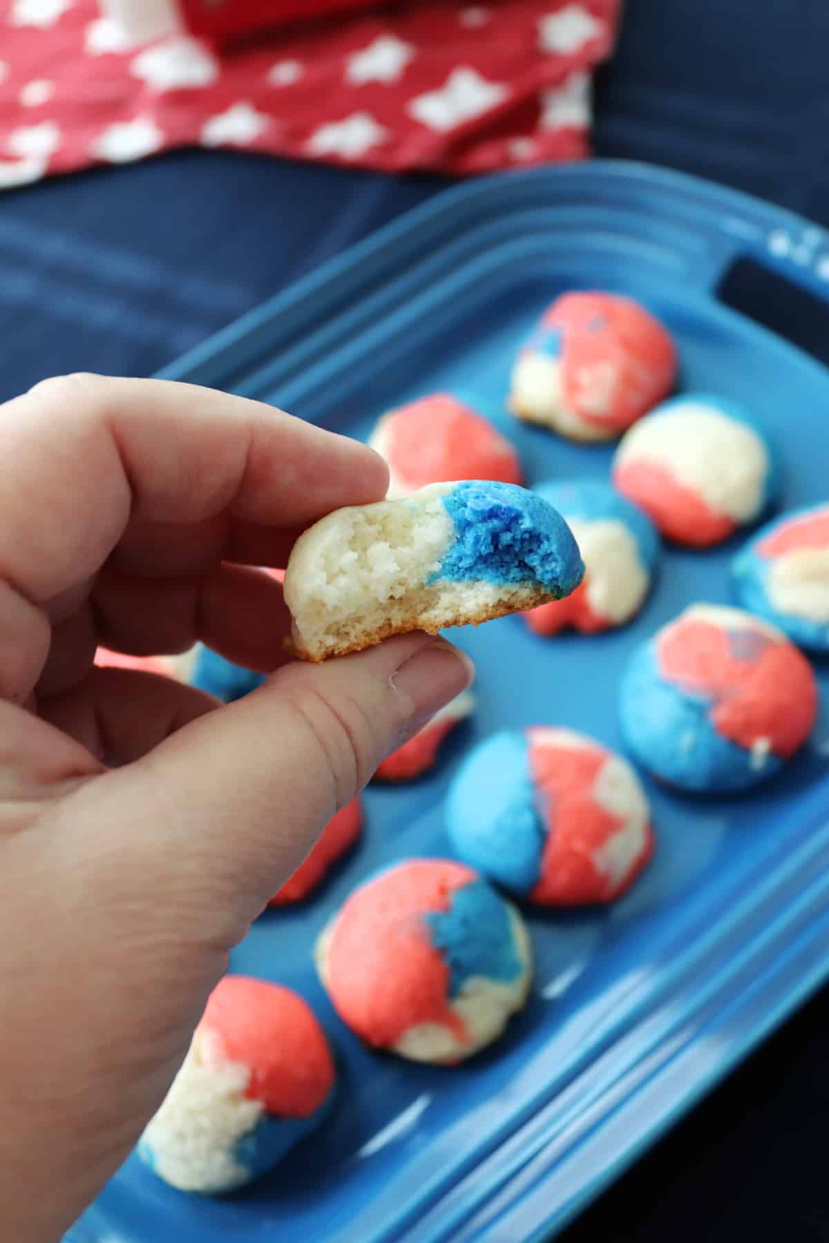 A hand holding a red, white, and blue cookie, exposing the inside, over a platter of more cookies.