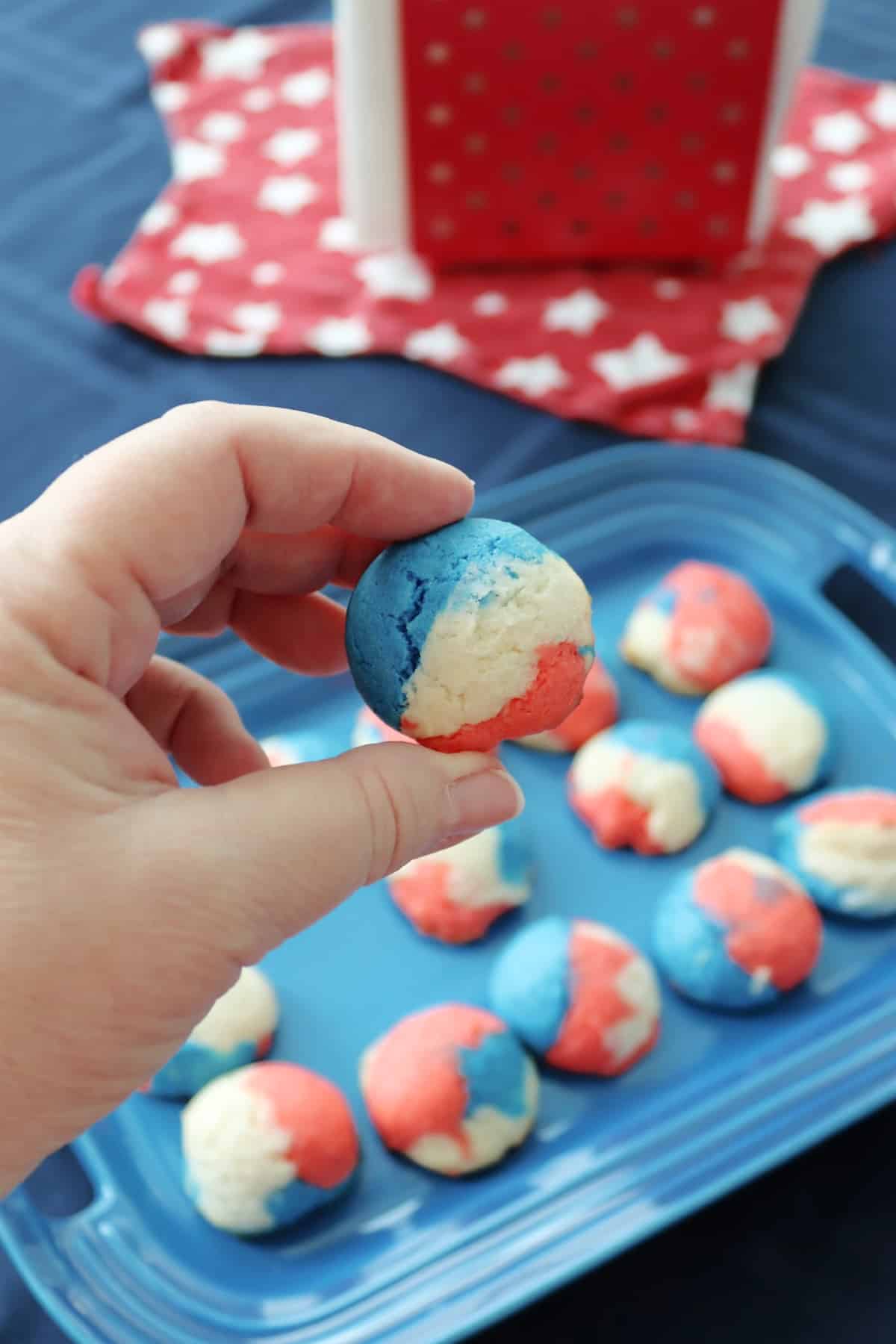 A red white and blue cookie being held over a platter with more cookies on it.