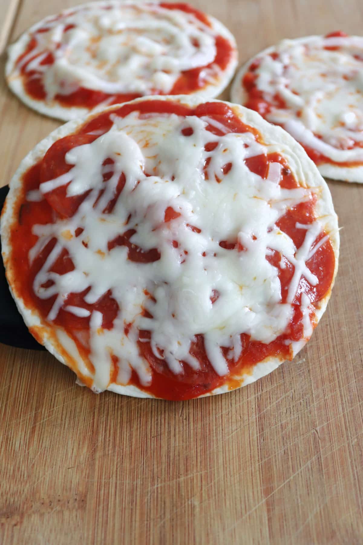 A tortilla pizza ona board with two more behind it.