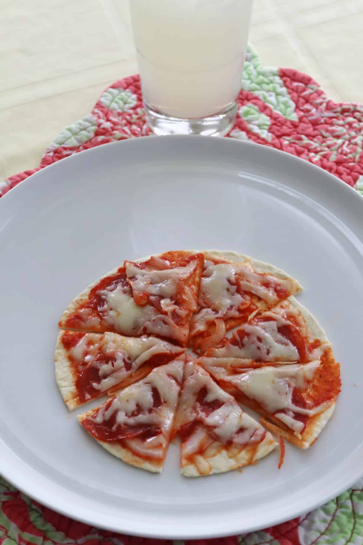 A tortilla pizza, cut into eight triangles, on a white plate.