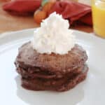 Chocolate chocolate chip pancakes stacked on a white plate topped with whipped cream.