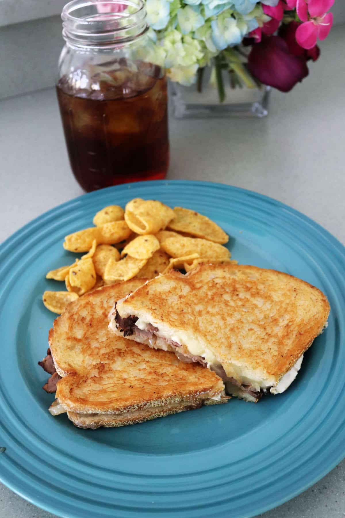 A grilled cheese sandwich on a blue plate with Fritos next to a glass of iced tea.
